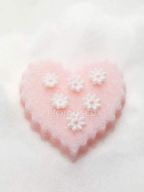 Primer plano vista superior del corazón de azúcar rosa con flores en la superficie blanca - foto de stock