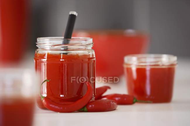 Pepper and chilli chutney in jars  on white surface — Stock Photo