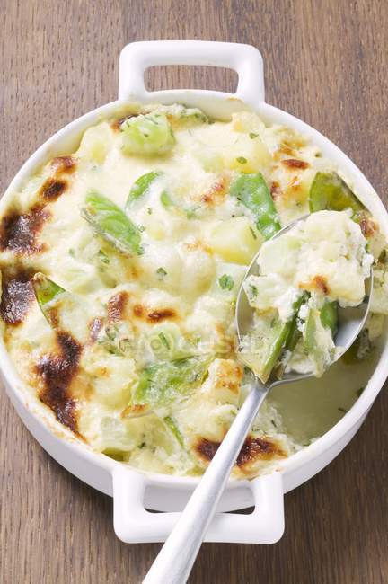 Potato gratin with mangetout in baking dish with spoon over wooden surface — Stock Photo
