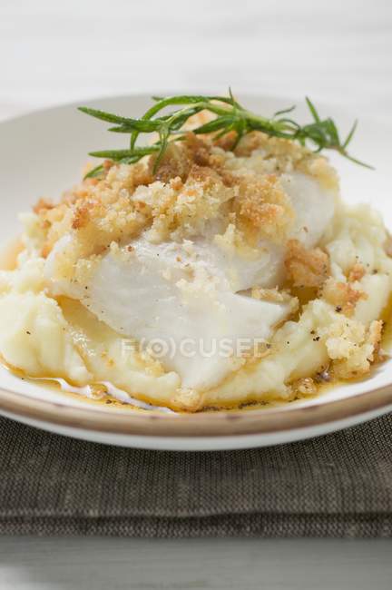 Eglefino con crosta di patate sul purè di patate in piatto bianco sopra asciugamano — Foto stock