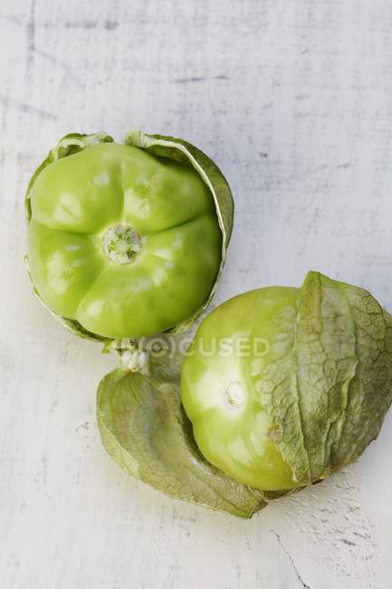 Два Tomatillos в оболочке над белой деревянной поверхностью — стоковое фото
