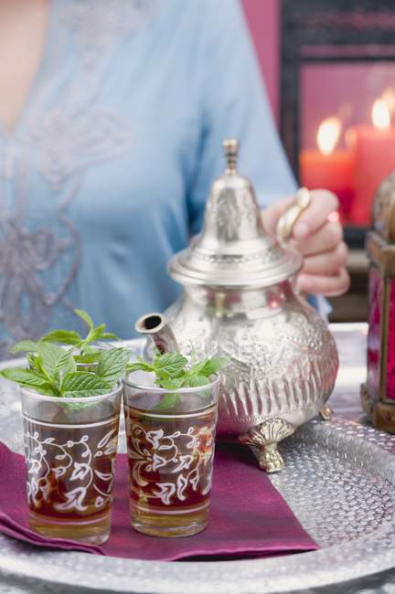 Cropped view of woman holding teapot by glasses of peppermint tea — Stock Photo
