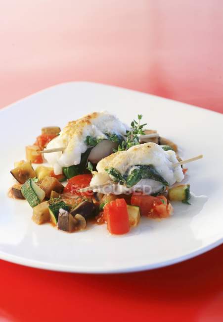 Monkfish on ratatouille in white plate over red surface — Stock Photo