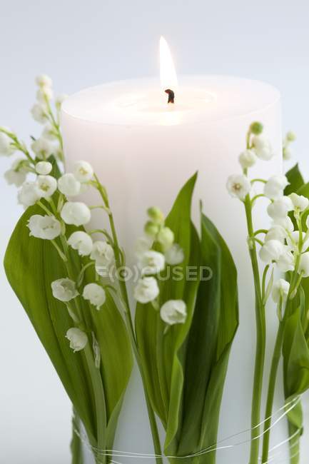 Closeup view of burning white candle with lilies of the valley — Stock Photo