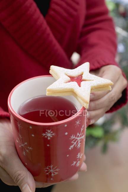 Cropped view of woman holding mug of tea with jam biscuit — Stock Photo