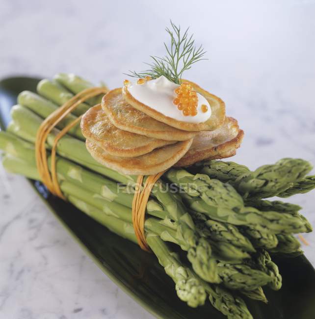 Blinis with sour cream and caviar on green asparagus — Stock Photo