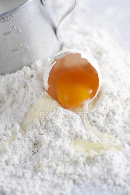 Vista de perto de ovo quebrado em monte de farinha com copo de medição — Fotografia de Stock