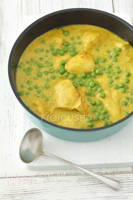 Chicken breast in curry sauce with peas in bowl over white wooden surface — Stock Photo