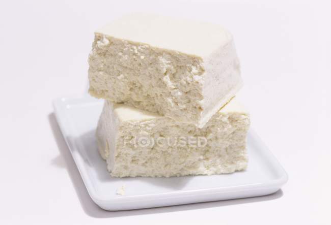 Крупный план нагроможденных кусочков сыра тофу на белом блюде — стоковое фото