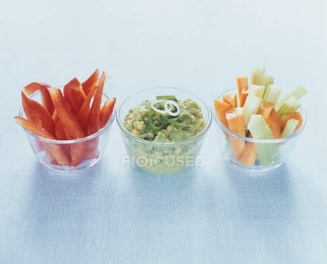 Palitos de verduras con guacamole en vasos sobre fondo azul - foto de stock