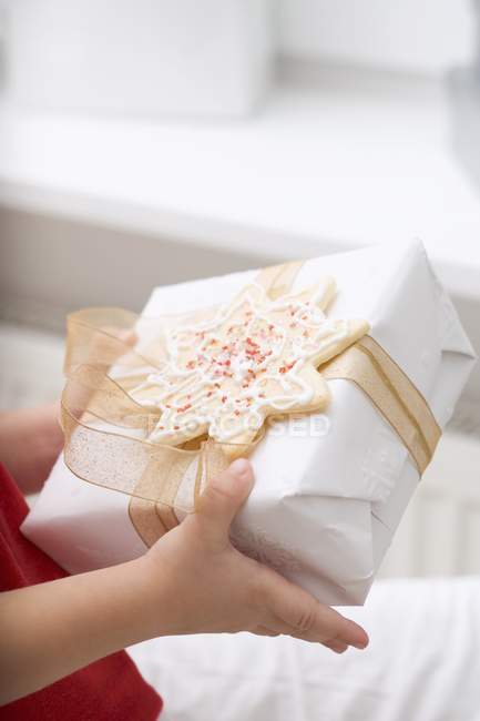 Child holding Christmas gift with star-shaped cookie — Stock Photo