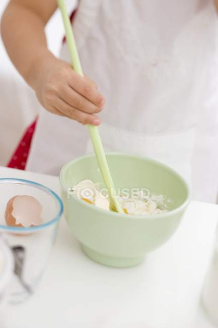 Vista de cerca de niña mezclando huevo, harina y mantequilla con cuchara de madera - foto de stock