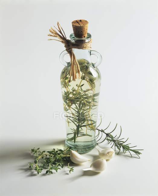 Nature morte avec du vinaigre de plantes dans une bouteille avec des herbes et de l'ail sur la surface blanche — Photo de stock