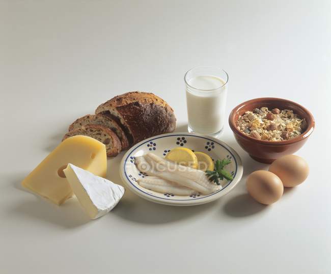 Elevated view of still life with cheeses, milk, eggs, bread and cereal on white surface — Stock Photo