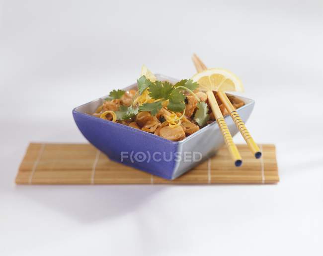 Pollo con limón, cebolla y cilantro en tazón azul sobre estera de paja - foto de stock
