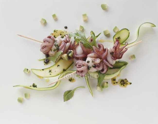 Nahaufnahme von aufgespießten Tintenfischen auf Zucchini-Bändern und gewürfelter Avocado — Stockfoto