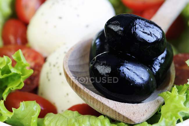 Черные оливки в деревянной ложке — стоковое фото