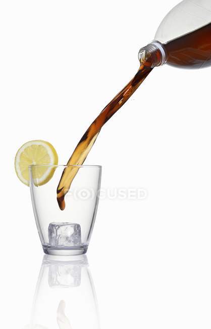 Vue rapprochée de verser du cola sur du verre avec glaçon et tranche de citron — Photo de stock