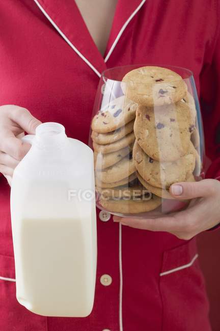 Close-up vista recortada de mulher segurando vidro de biscoitos de cranberry e garrafa de leite — Fotografia de Stock