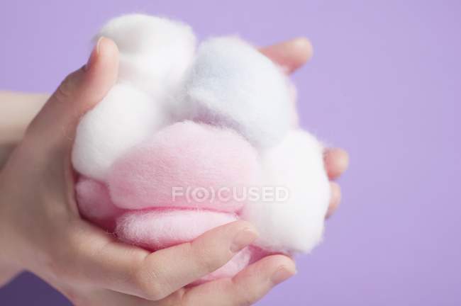 Vista de cerca de las manos sosteniendo bolas de algodón blanco y rosa - foto de stock