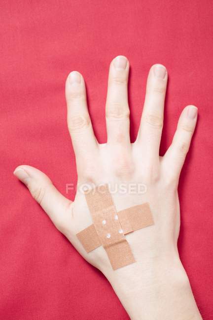 Hand mit überkreuzten Klebepflastern auf roter Oberfläche — Stockfoto