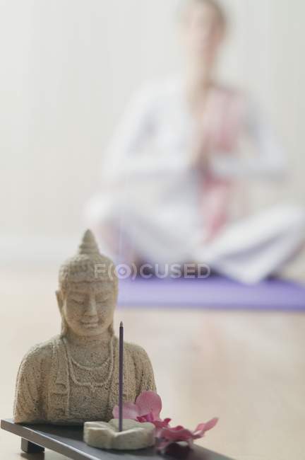 Buddha-Statue und Räucherstäbchen mit Frau im Schneidersitz auf dem Hintergrund — Stockfoto