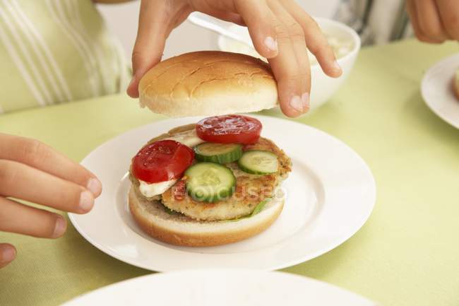 Vue rapprochée des mains préparant un hamburger de poisson avec des légumes — Photo de stock