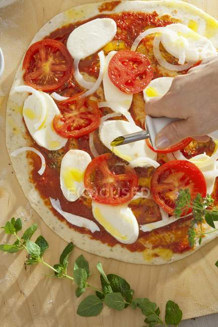 Sprinkling pizza with olive oil — Stock Photo