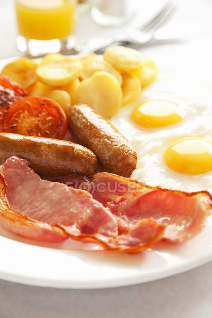 Close up view of English breakfast with sausages, bacon, fried eggs and vegetables — стоковое фото