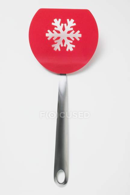 Closeup top view of red spatula with snowflake shaped perforation on white surface — Stock Photo