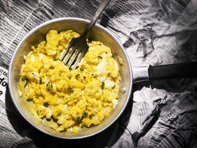 Top view of scrambled egg in a small frying pan with a fork on a newspaper — Stock Photo
