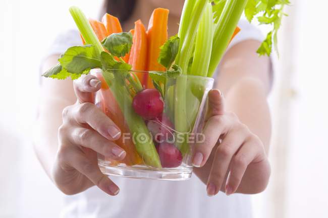 Fille tenant un bol de bâtonnets de légumes avec des radis, section médiane — Photo de stock