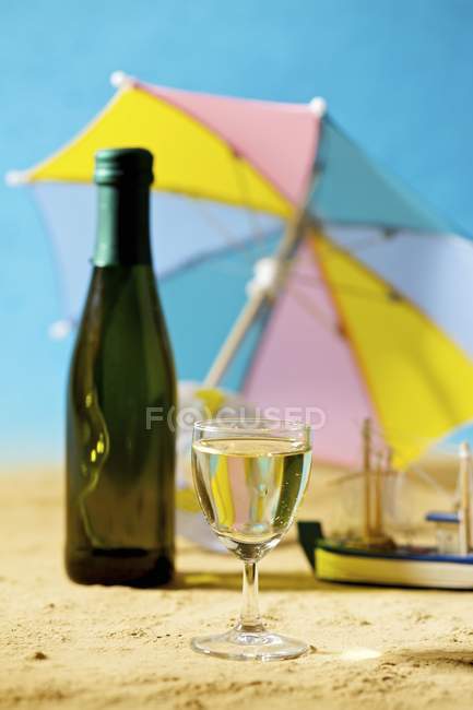Vista de cerca de la copa y la botella de vino blanco en la playa de arena - foto de stock
