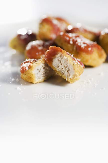 Vista de cerca de nuggets de pollo enteros y cortados a la mitad con ketchup - foto de stock