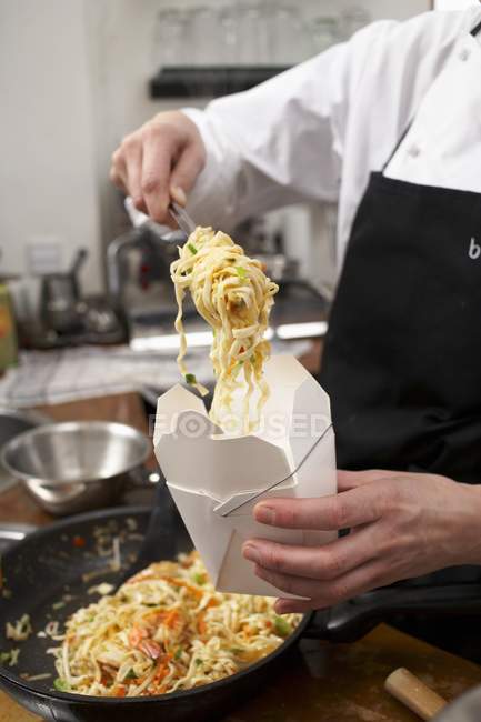 Cook filling box with noodles — Stock Photo