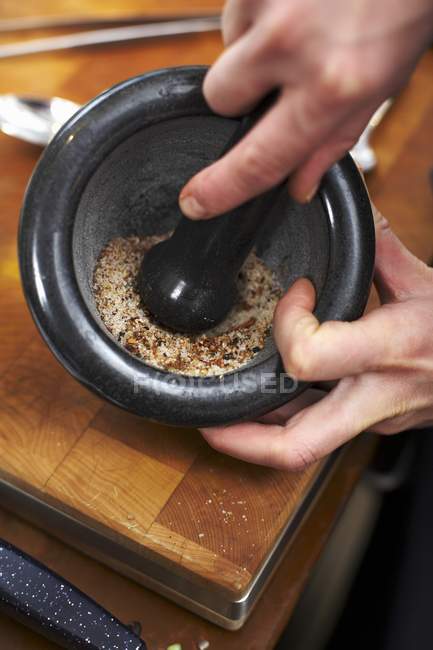 Vista de cerca de las manos pulverizando sal sazonada en un mortero - foto de stock