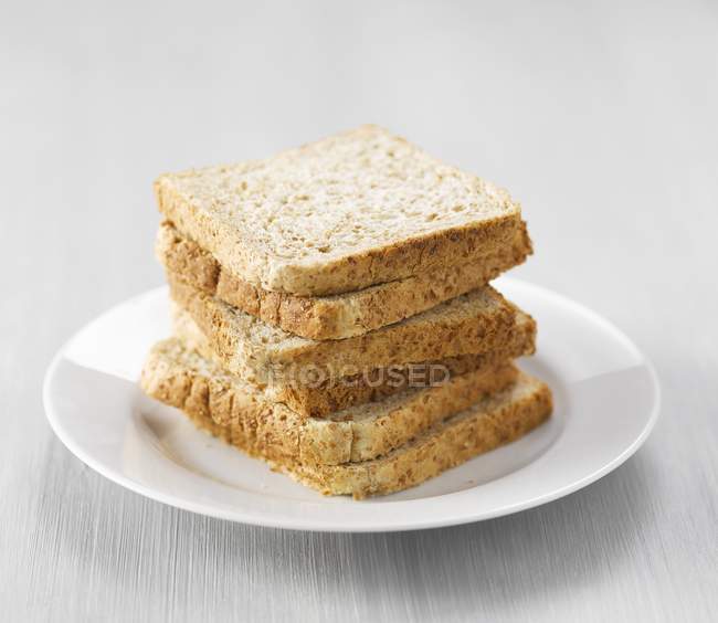 Closeup view of stacked wholemeal toasts on white plate — Stock Photo