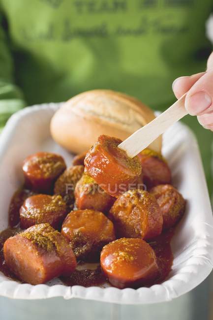 Vue rapprochée de la personne avec Currywurst sur une fourchette en bois — Photo de stock