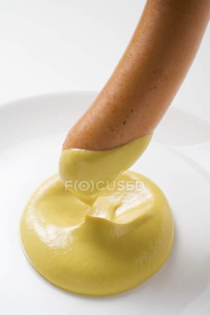 Dipping sausage in mustard — Stock Photo
