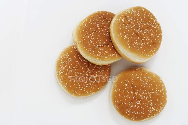 Top view of four hamburger buns with sesame seeds on white surface — Stock Photo