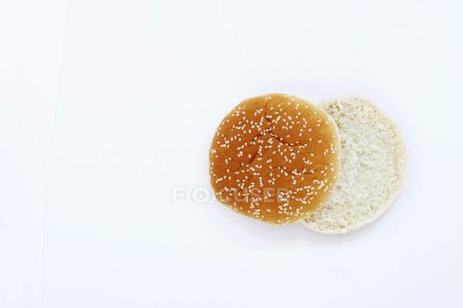 Vista superior de un bollo de hamburguesa en rodajas con sésamo en la superficie blanca - foto de stock