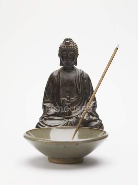Palo de incienso ahumado en plato de cerámica frente a la figura de Buda - foto de stock