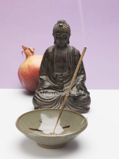 Closeup view of incense stick in ceramic dish with Buddha figure and pomegranate — Stock Photo