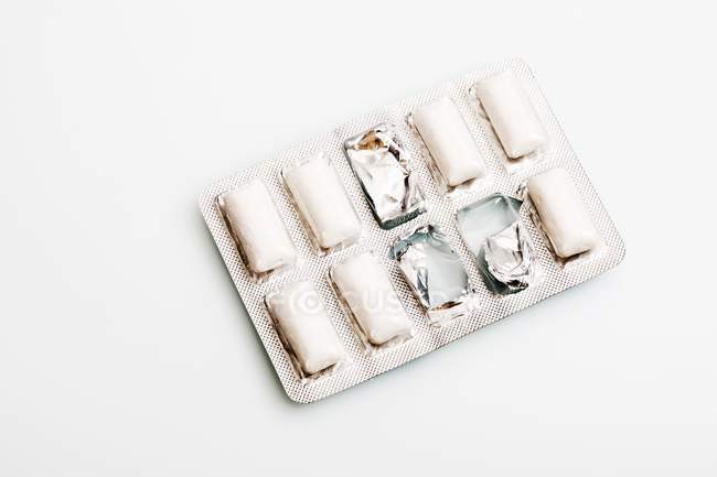Vue rapprochée des granulés de gomme à mâcher dans l'emballage sur une surface blanche — Photo de stock