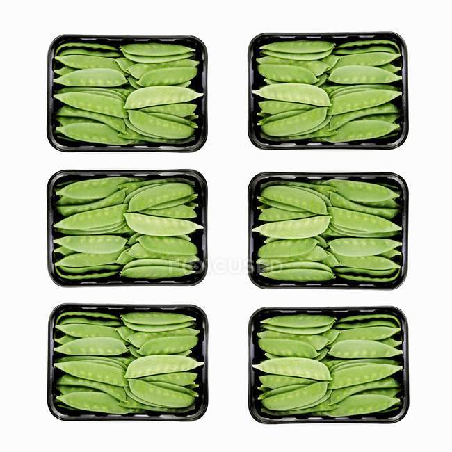 Mangetout in sechs Plastiktabletts auf weißem Hintergrund — Stockfoto