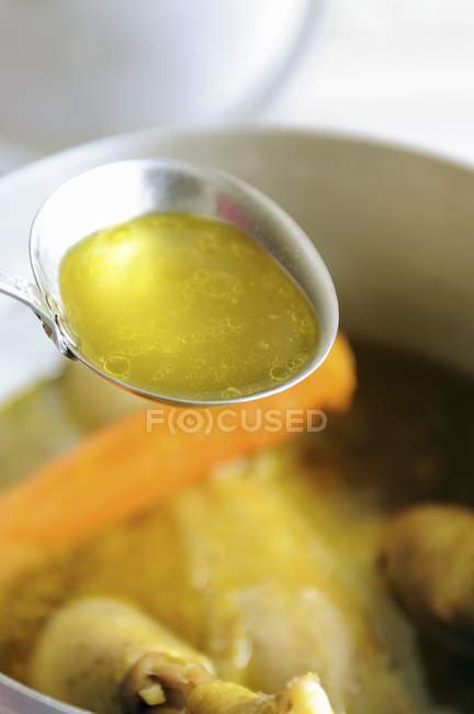 Cucharón de caldo de pollo sobre olla de sopa - foto de stock