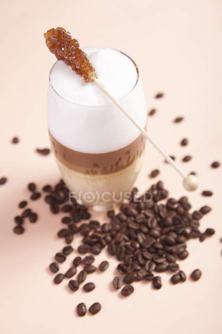 Vue rapprochée de Latte stratifié avec bâton de sucre et grains de café — Photo de stock