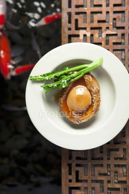 Abalone  on white plate over decorative wooden table — Stock Photo
