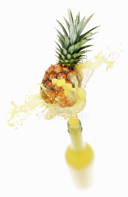 Pineapple juice splashing out of bottle — Stock Photo