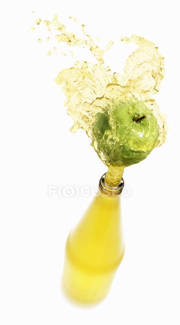 Apple juice splashing out of bottle — Stock Photo